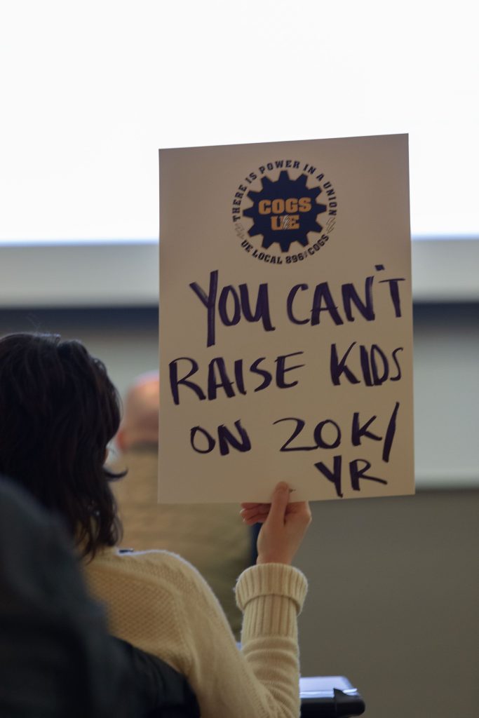A COGS member holds a sign during bargaining that reads, "You can't raise kids on 20 k per year."